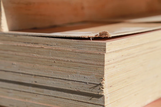 Close-up of skilled hands inspecting a smooth plywood sheet in a warmly lit factory setting.