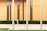 A woman walks along a paved sidewalk in front of a modern building with vertical orange panels and a row of windows. Three metallic poles stand in the forefront, and there is a well-maintained hedge lining the base of the building. The text 'FINANCIAL CENTER' is visible on the building.