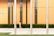 A woman walks along a paved sidewalk in front of a modern building with vertical orange panels and a row of windows. Three metallic poles stand in the forefront, and there is a well-maintained hedge lining the base of the building. The text 'FINANCIAL CENTER' is visible on the building.