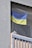 A blue and yellow flag is hanging behind a safety net on a balcony. The balcony is part of a building with a textured gray wall and vertical railing bars.