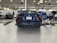 A dark-colored car parked inside a large, well-lit garage or workshop. The vehicle is facing away, showing a detailed view of its rear with a visible license plate. The garage is equipped with various tools, equipment, and machinery such as toolboxes, jacks, and oil containers. The space is organized with items placed neatly along the walls and on workbenches.