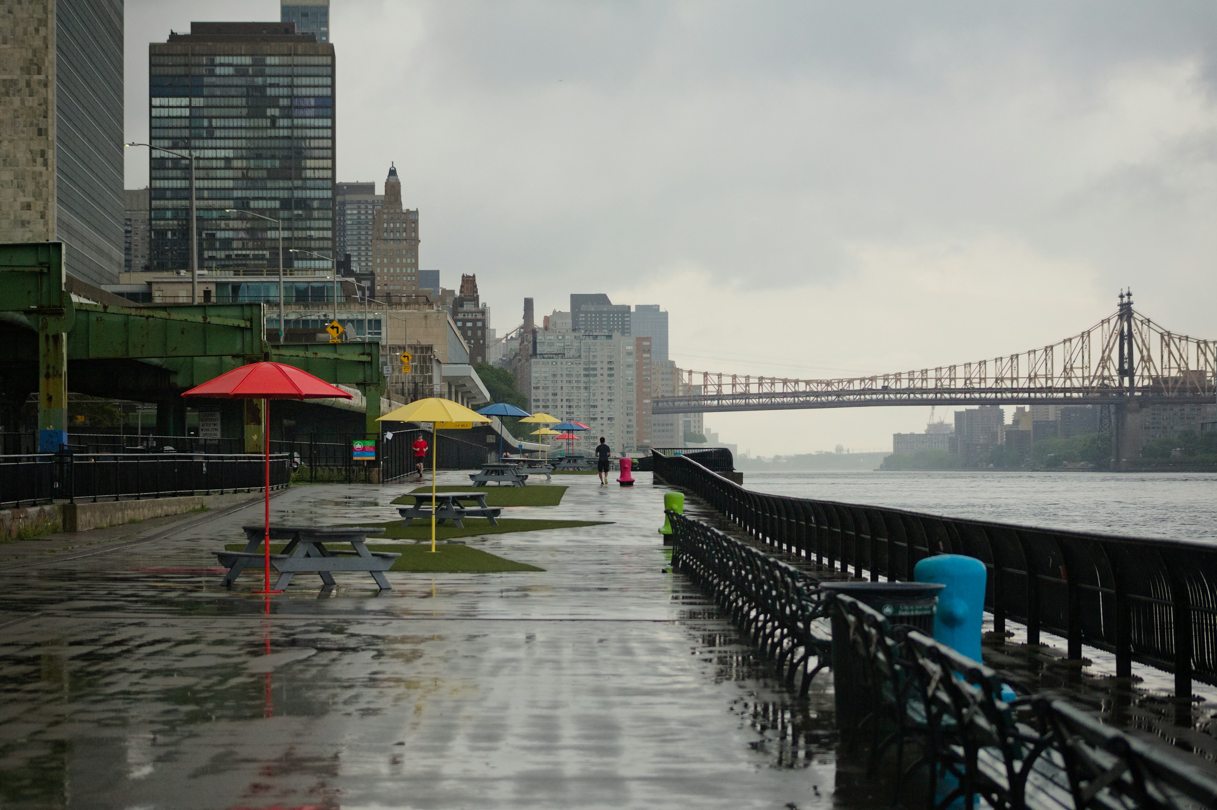 a city street with benches and umbrellas on a rainy day