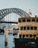 A ferry named Scarborough is docked in the foreground with a visible Transport Sydney Ferries logo. The iconic Sydney Harbour Bridge looms in the background, with a cityscape of tall buildings partially obscured by the bridge's steel structure. Two flags are flying at the top of the bridge, and another ferry is seen in the midground navigating through the water.