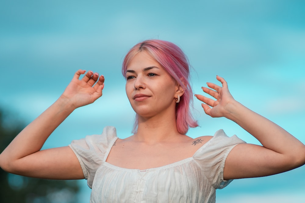 a woman with pink hair is holding her hands up