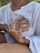 Hands gently rest on a person's chest, creating a sense of comfort and connection. The person is wearing a white textured garment, and there's a red bracelet on one of the hands. The scene is intimate, emphasizing human touch and emotion.