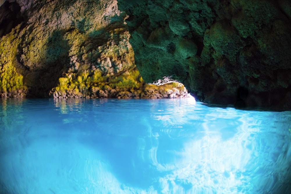 uma caverna com água azul e rochas verdes