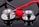 Two stethoscopes with shiny metallic diaphragms are arranged on a reflective black surface, with a small red heart placed in the center between them.