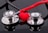 Two stethoscopes with shiny metallic diaphragms are arranged on a reflective black surface, with a small red heart placed in the center between them.