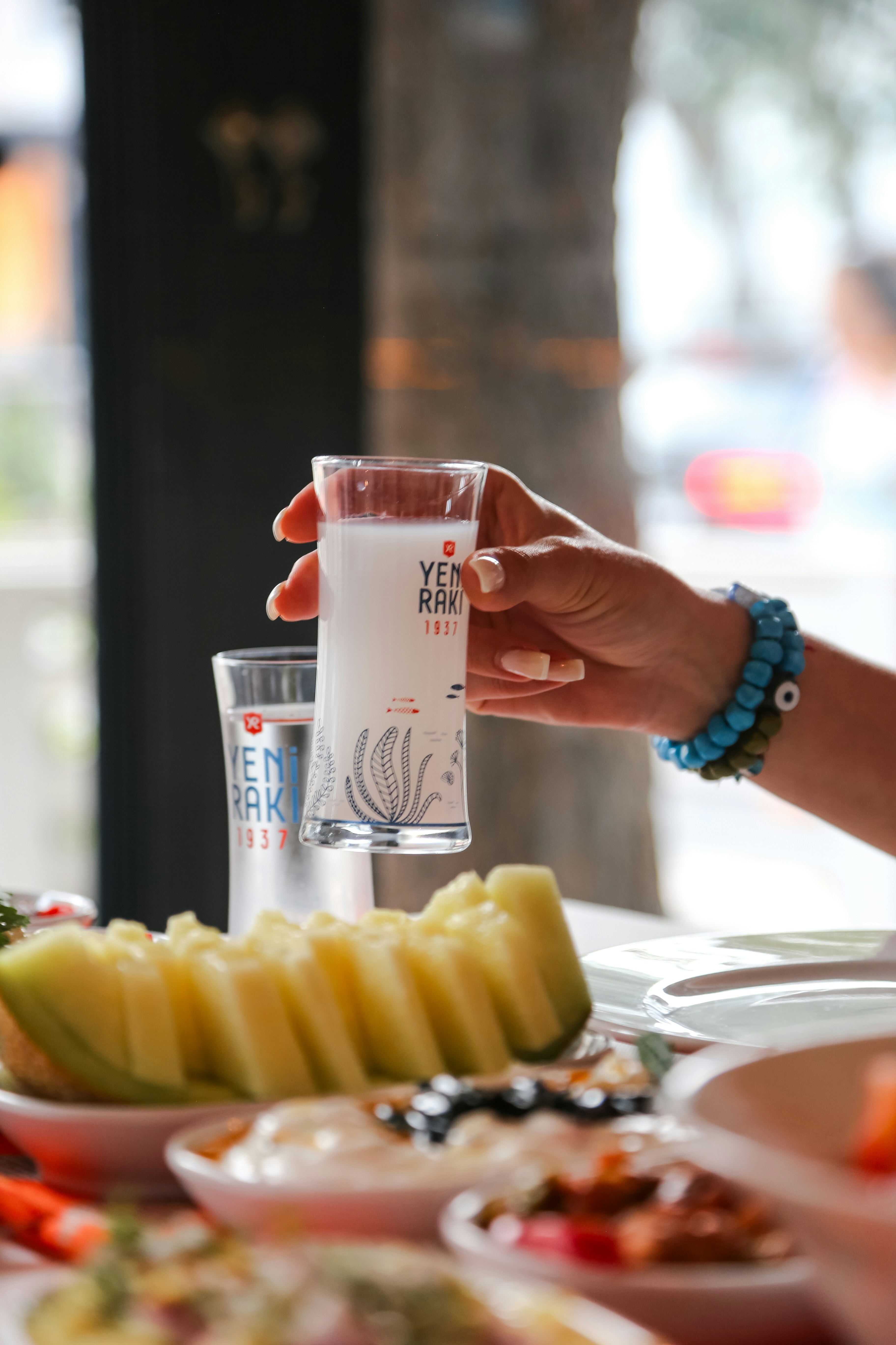 a woman holding a glass of water over a plate of food