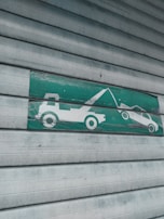 A green and white sign indicating a tow truck pulling a car, mounted on a corrugated metal shutter with a textured, weathered appearance.