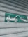 A green and white sign indicating a tow truck pulling a car, mounted on a corrugated metal shutter with a textured, weathered appearance.