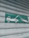 A green and white sign indicating a tow truck pulling a car, mounted on a corrugated metal shutter with a textured, weathered appearance.