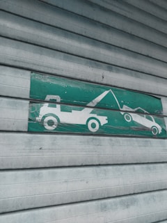 A green and white sign indicating a tow truck pulling a car, mounted on a corrugated metal shutter with a textured, weathered appearance.