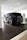 A sleek black Volkswagen ID.3 electric car is displayed inside a modern showroom with bright lighting. The vehicle is positioned on a raised platform beneath a white ceiling, with reflective surfaces highlighting its glossy finish. Nearby, a charging station marked with the Ohme logo is visible.