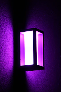 A sleek black 3D-printed lamp casting a soft purple glow on a dark charcoal surface.