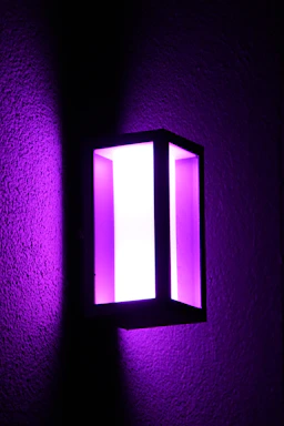 A sleek black 3D-printed lamp casting a soft purple glow on a dark charcoal surface.