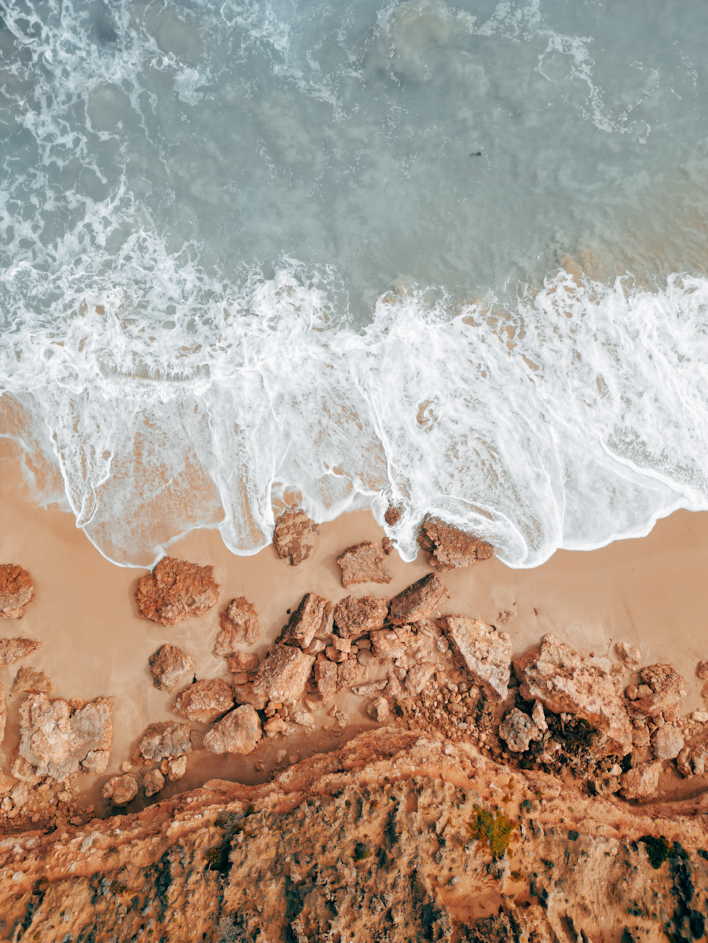 an aerial view of a beach with waves and rocks