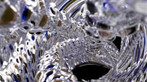 An abstract image featuring swirling, metallic-like textures with reflective surfaces and intricate, looping patterns. The design creates a sense of depth and movement, with hints of blue and silver tones.