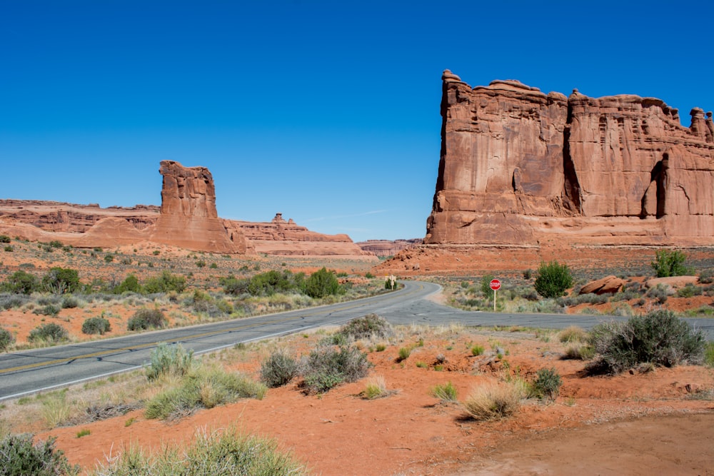 a road in the middle of a desert with a rock formation in the background