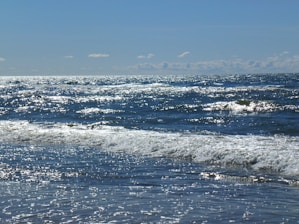 Sunlight sparkling on gentle ocean waves with a clear blue sky.