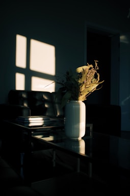 A sleek modern coffee table with a glass top, styled with a vase of fresh flowers and books.