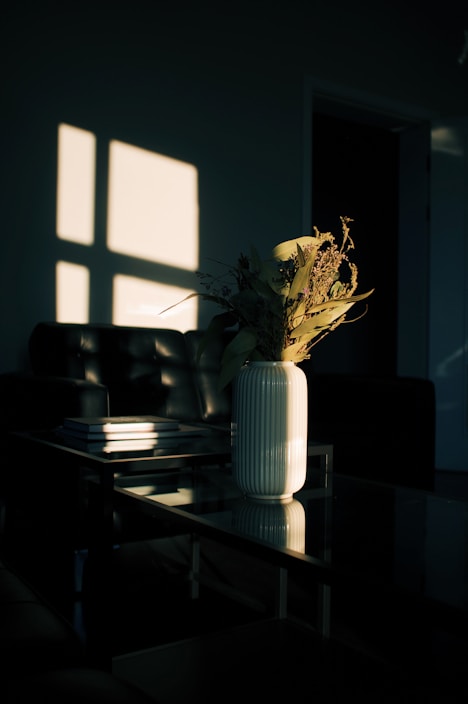 A sleek modern coffee table with a glass top, styled with a vase of fresh flowers and books.