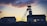A silhouetted industrial structure stands against a dramatic sunset sky, with hues of orange and purple. The building appears to be a mining facility with a tall headframe, and there is also a secondary building with a pitched roof visible.