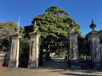 A striking entranceway combining raw stone pillars with sleek metal accents, nestled among mature trees.