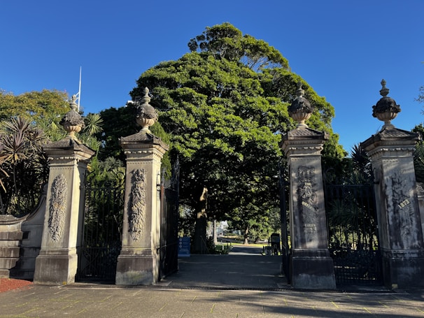 A striking entranceway combining raw stone pillars with sleek metal accents, nestled among mature trees.