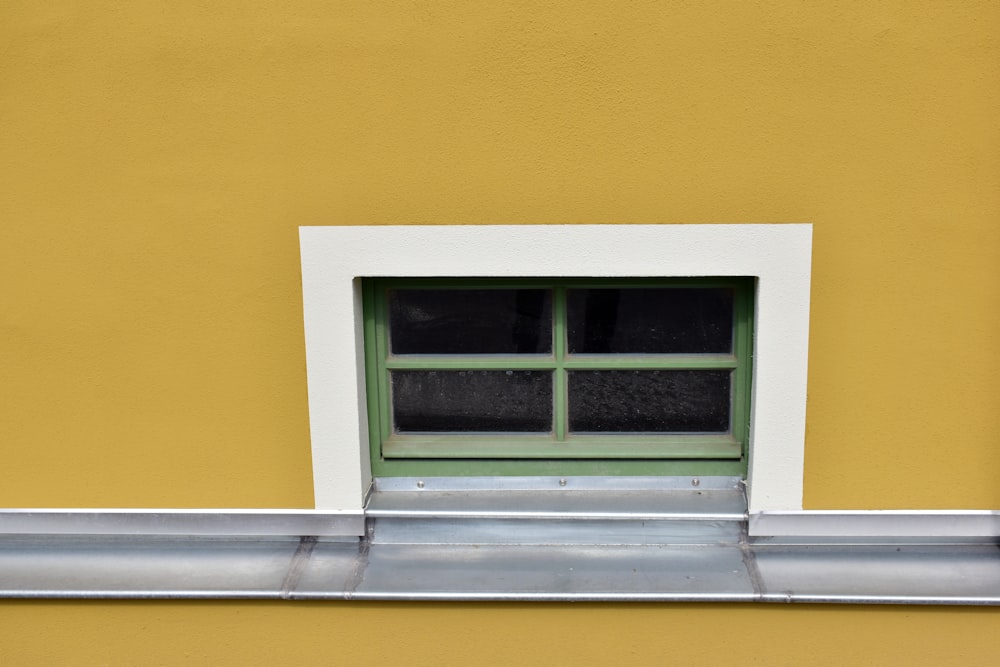 a yellow building with a green window and a metal gutter