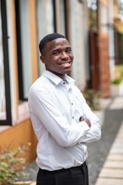 A confident professional standing outdoors, smiling with arms crossed.