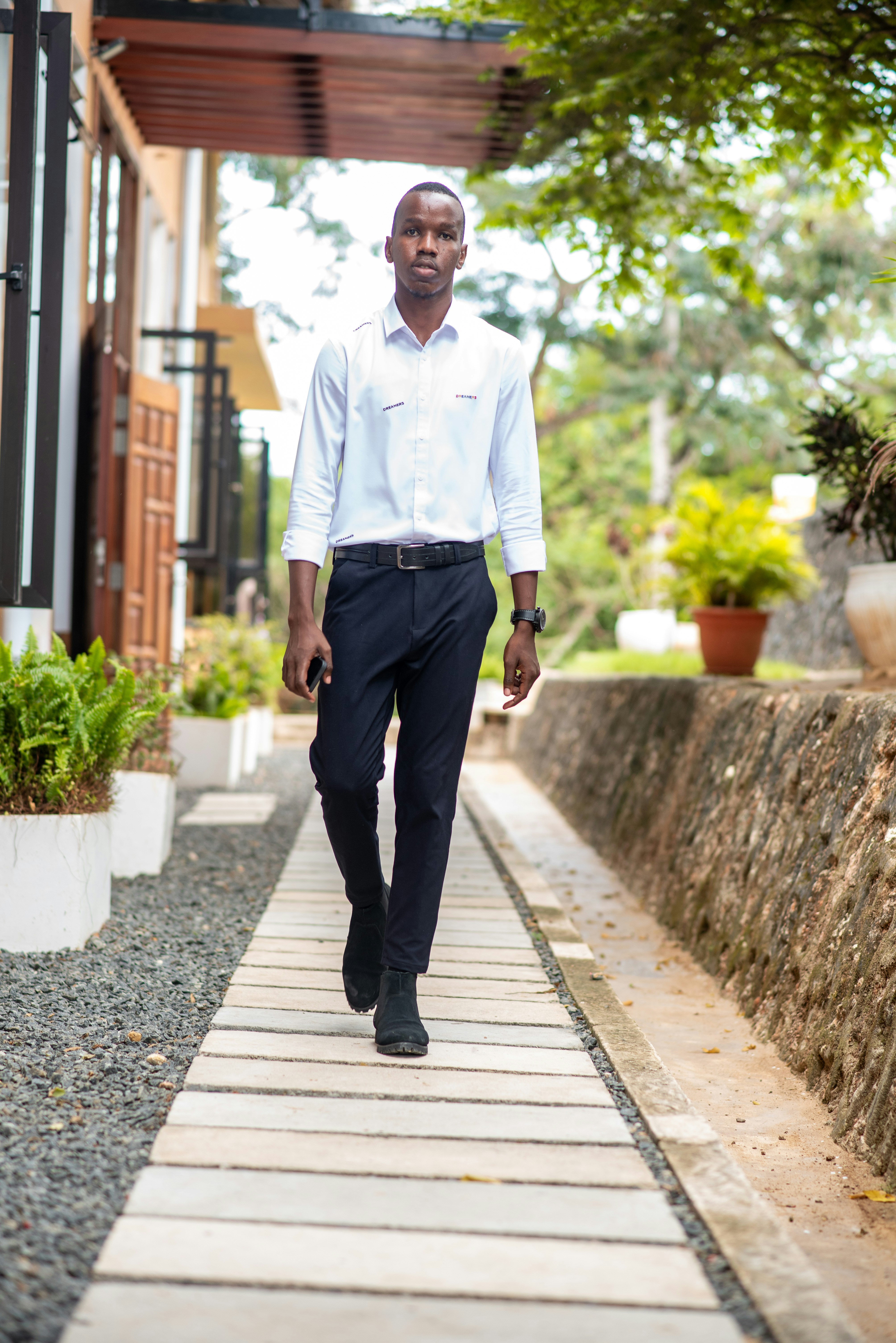a man in a white shirt and black pants walking down a sidewalk