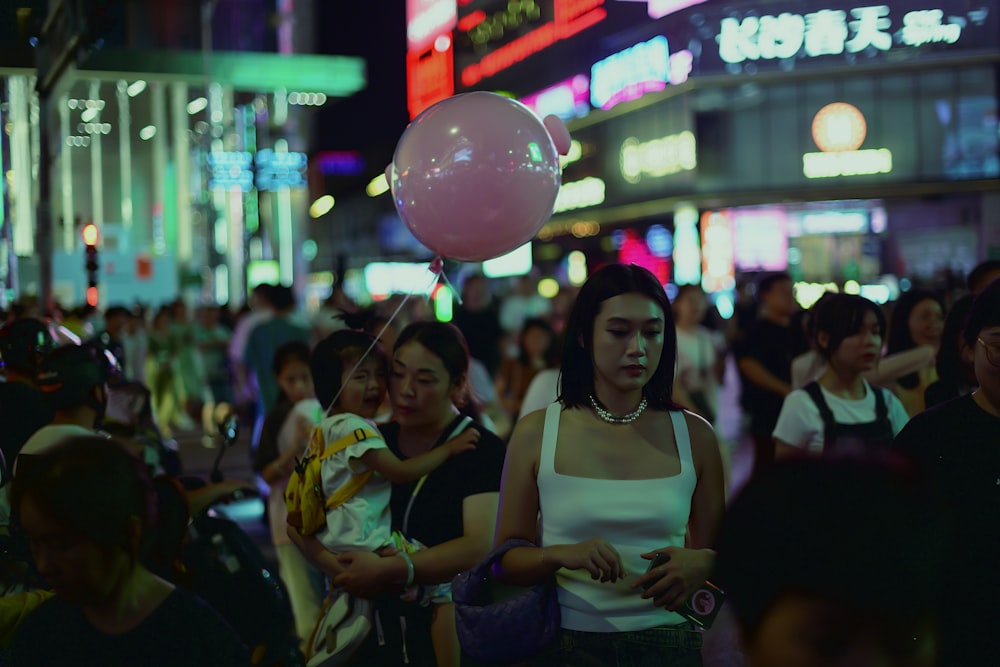a woman holding a pink balloon in the middle of a crowded street