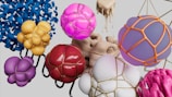 An abstract composition featuring various spherical and amorphous shapes, some encapsulated in metallic wireframes. These shapes are in vibrant hues like pink, purple, yellow, and red, and are set against a neutral background. The designs evoke a sense of flowing motion and artistic creativity.