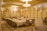 An opulent banquet hall adorned with ornate chandeliers and intricate architectural designs. The room is primarily decorated in soft beige and gold tones, with luxurious draped curtains and a lavishly set dining table surrounded by ornate chairs. The geometric patterns on the ceiling and arches contribute to the grandeur.