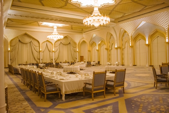 A grand banquet hall adorned with royal decor, softly lit chandeliers casting a warm glow over elegantly set tables.