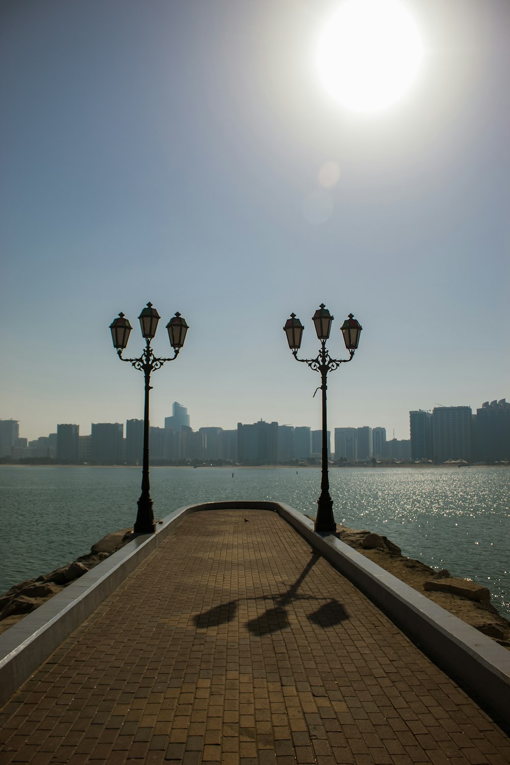 the sun is shining over the water and a brick walkway