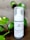 A bottle of charcoal cleanser with a white label and a pump dispenser, set against a neutral background. The product is surrounded by green leafy plants, adding a natural touch to the scene.
