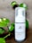 A bottle of charcoal cleanser with a white label and a pump dispenser, set against a neutral background. The product is surrounded by green leafy plants, adding a natural touch to the scene.