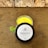 A jar of saffron cream with a bright yellow color is placed on a brown textured surface. The lid is off to the side and displays the label 'maya, Saffron Cream, 100% Natural, Net Wt. 50 gms.' A small green leaf is nearby, adding a natural element. The background features a stone wall with a rough texture.