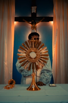 A close-up of a glowing monstrance holding the Eucharist, bathed in soft candlelight.