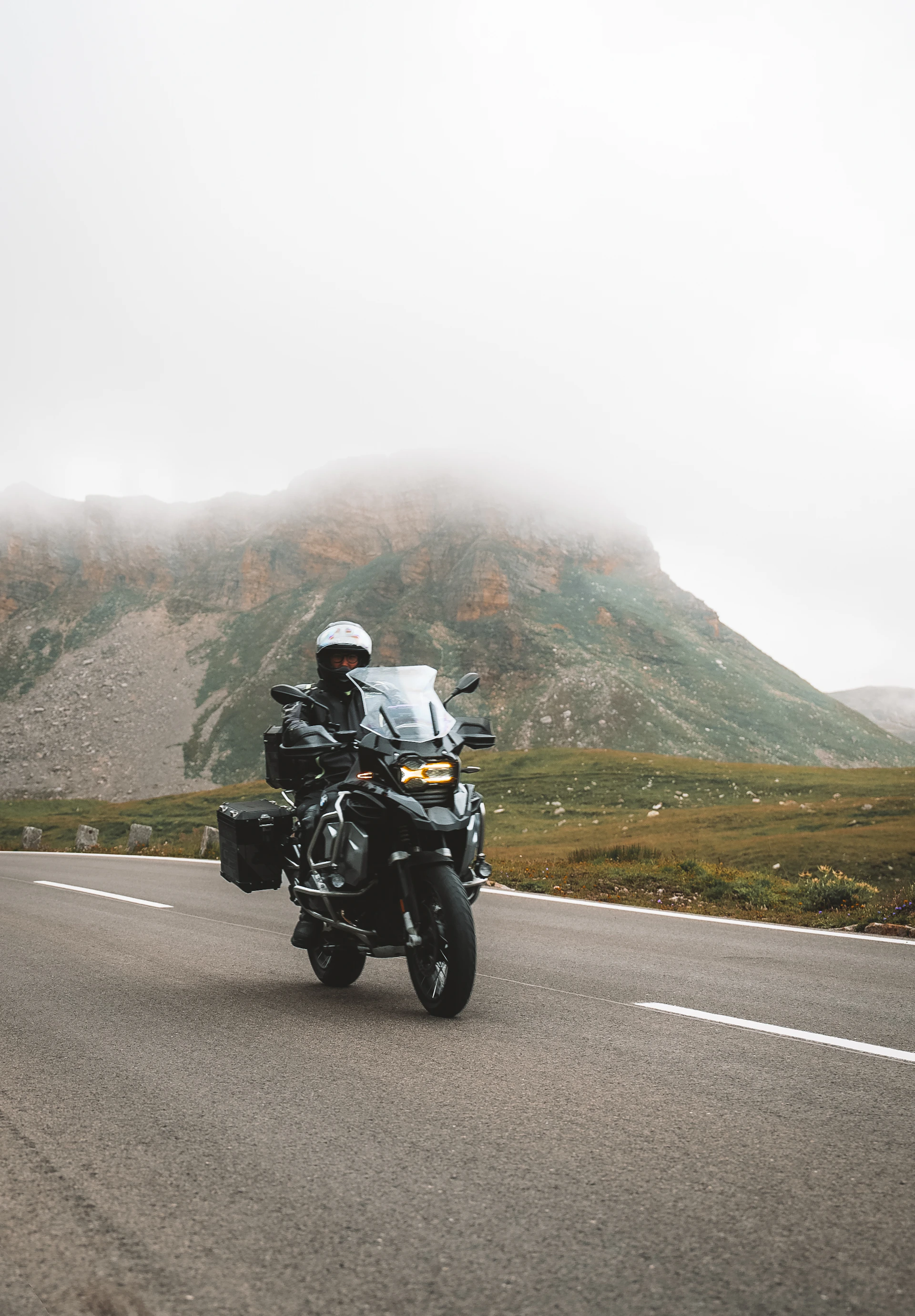 a man riding a motorcycle down a road next to a mountain