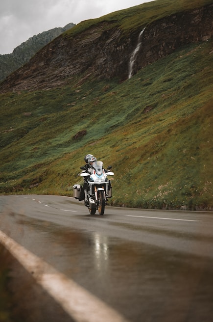 A rider cruising along a winding mountain road with autumn leaves around