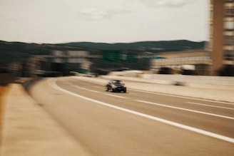 A modern car driving on a highway with mountains in the background.