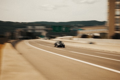 A modern car driving on a highway with mountains in the background.