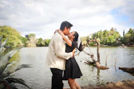 A same-sex couple sharing a tender kiss by a serene lake surrounded by lush greenery.