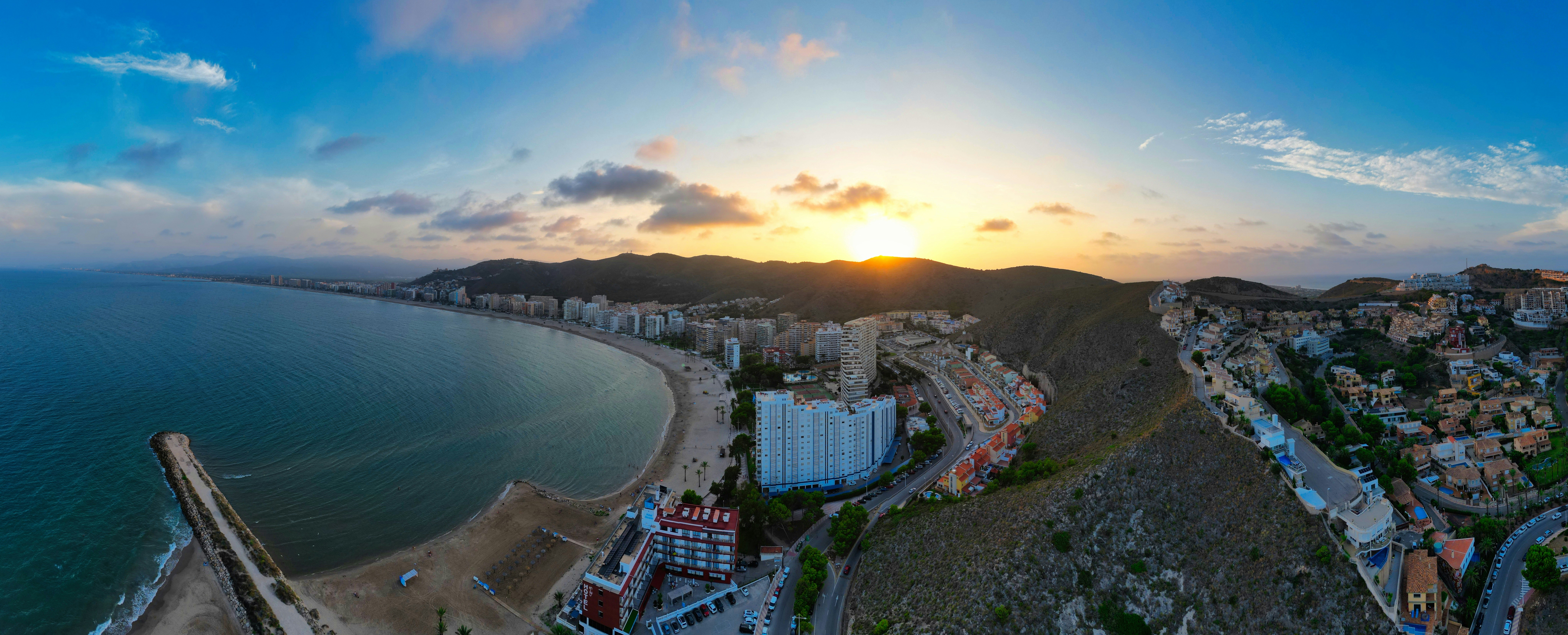 the sun is setting over a city by the ocean