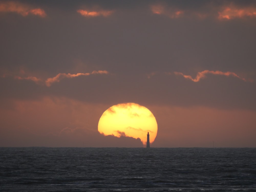 the sun is setting over the ocean with a sailboat in the distance