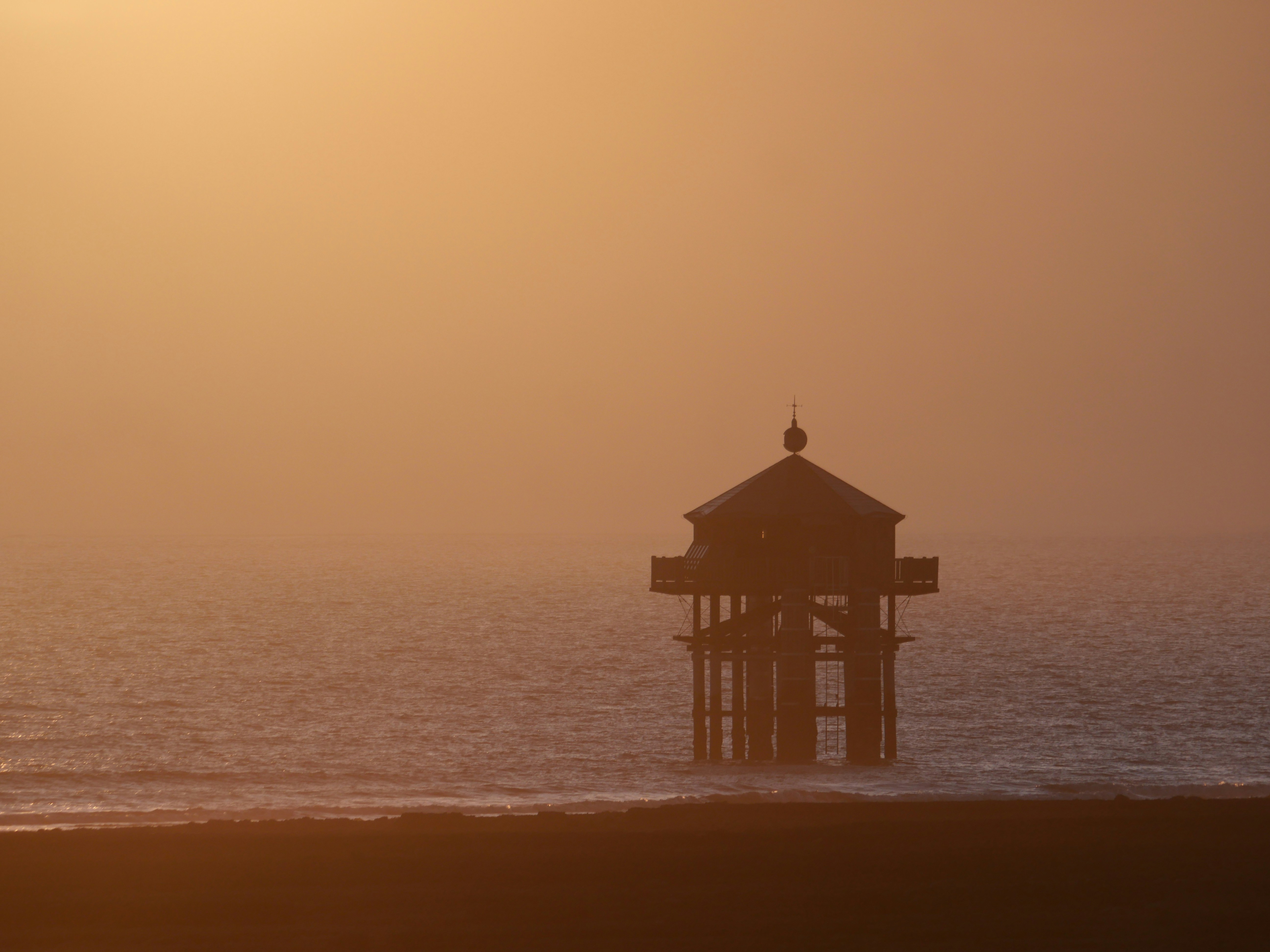Una pequeña torre en una playa con el sol de fondo