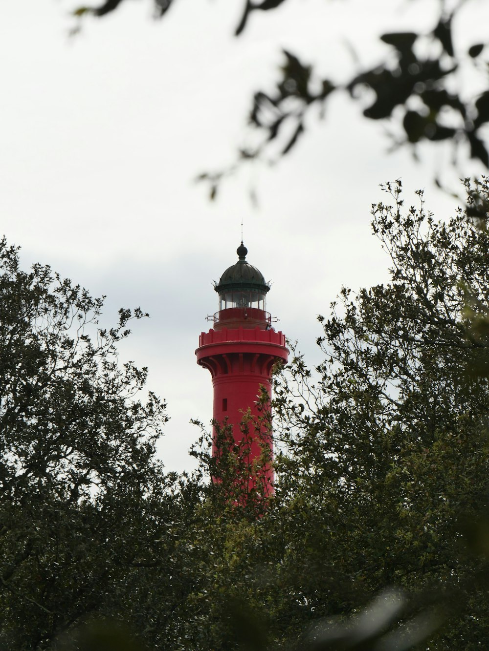 a red light house surrounded by trees on a cloudy day